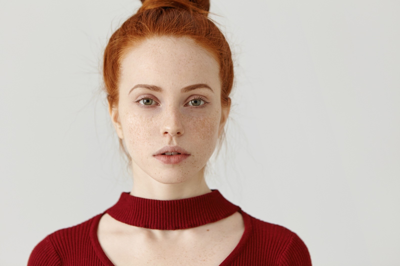 Close up shot of gorgeous young Caucasian woman with perfect freckled skin and ginger hair looking at camera with subtle smile, wearing beautiful maroon dress with cut out before going to party